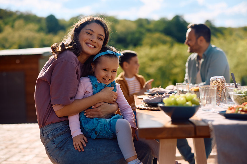 Rodinné posezení u stolu s čerstvými farmářskými produkty na slunné zahradě